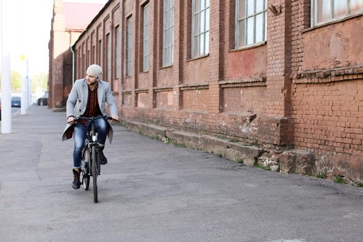 Handsome young man in grey coat and hat riding a bicycle street in the city