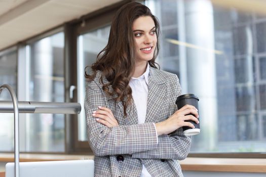 Attractive smiling businesswoman standing in the office with a cup of coffee