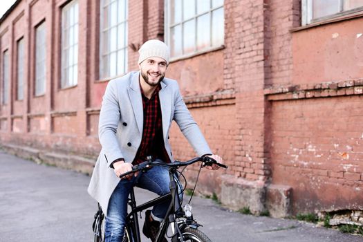 Handsome young man in grey coat and hat riding a bicycle street in the city