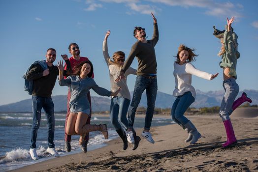 Group of excited young friends jumping together at sunny autumn beach