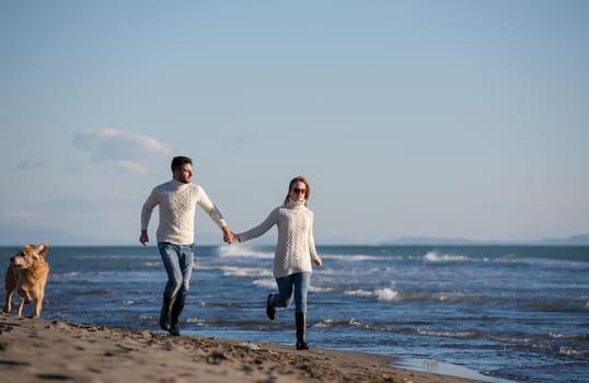 Couple Running On The Beach Holding Their Hands with dog On autmun day