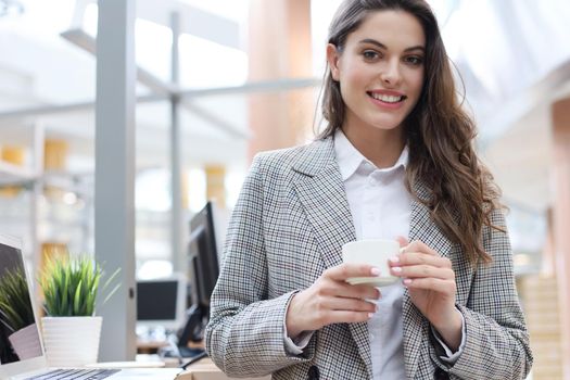 Attractive smiling businesswoman standing in the office with a cup of coffee