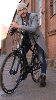 Handsome young man in grey coat and hat standing with his bicycle