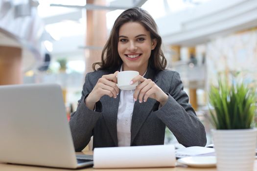 Attractive smiling businesswoman sitting in the office with a cup of coffee