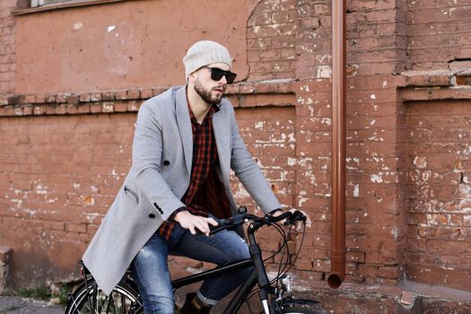 Handsome young man in grey coat and hat riding a bicycle street in the city