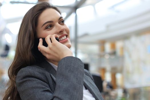 Young smiling business woman using smartphone near computer in office