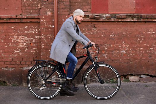 Handsome young man in grey coat and hat standing with his bicycle