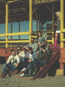 Happy Group Of Friends Hanging Out At Beach House having fun and drinking beer on autumn day colored filter