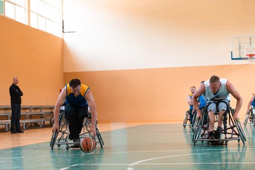 Disabled War or work veterans mixed race and age basketball teams in wheelchairs playing a training match in a sports gym hall. Handicapped people rehabilitation and inclusion concept.Hi quality photo