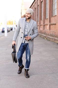 City life. Stylish young man in grey coat and hat walking on the street in the city