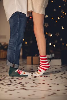 Crop of couple tiptoes to kiss wearing festive Christmas socks,