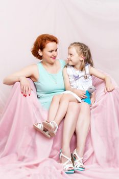 Mom and daughter are sitting on the couch. The concept of family happiness, parenthood, childhood. Isolated on white background.