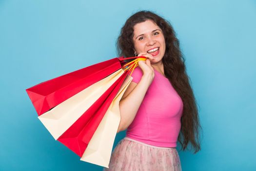 Portrait of young happy smiling woman with shopping bags, over blue background. Purchase, sale and people concept.