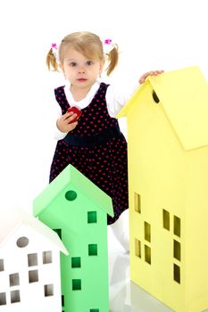 A cute little girl is playing with wooden houses. The concept of family happiness, play, creative development of the child.