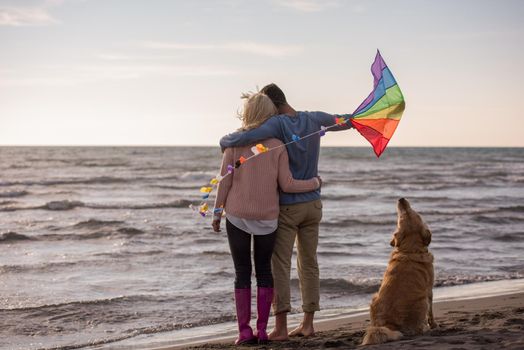 Young Couple having fun playing with a dog and Kite on the beach at autumn day