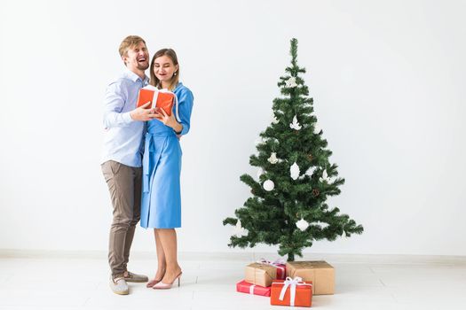 Holidays and festive concept - Young happy couple near a Christmas tree on white background.