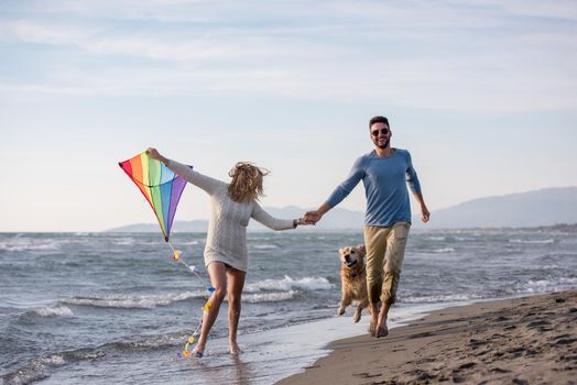 Young Couple having fun playing with a dog and Kite on the beach at autumn day