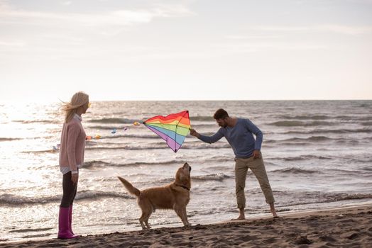 Young Couple having fun playing with a dog and Kite on the beach at autumn day