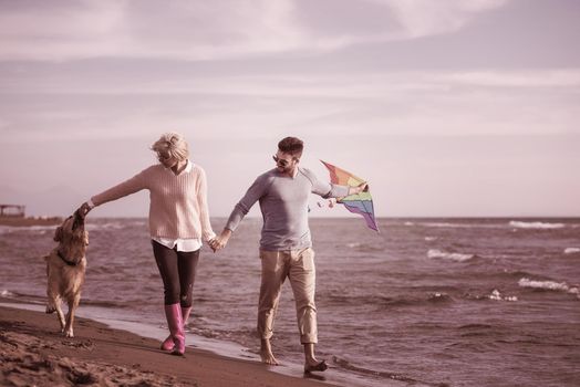 Young Couple having fun playing with a dog and Kite on the beach at autumn day filter