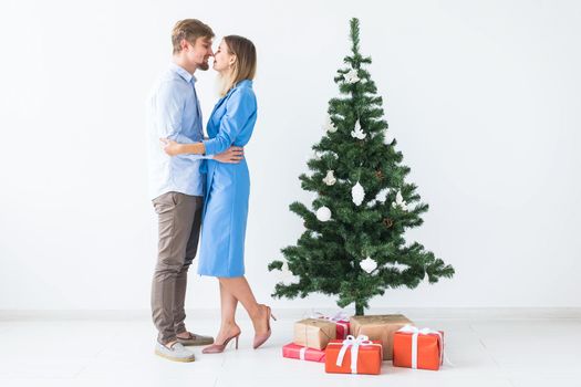 Holidays and festive concept - Young happy couple near a Christmas tree on white background.
