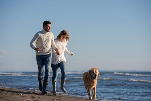 Couple Running On The Beach Holding Their Hands with dog On autmun day