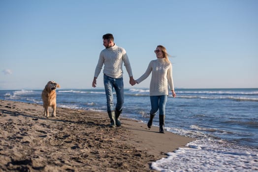 Couple Running On The Beach Holding Their Hands with dog On autmun day