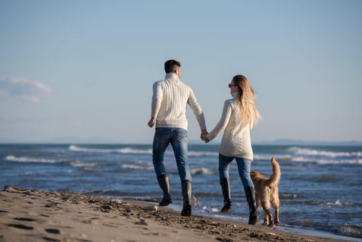 Couple Running On The Beach Holding Their Hands with dog On autmun day