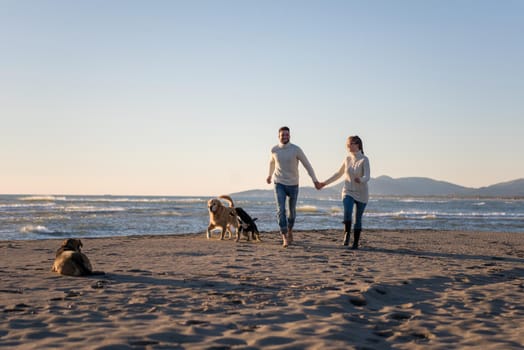 Couple Running On The Beach Holding Their Hands with dog On autmun day