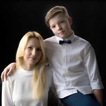 Mom and son teenager on a black background. The concept of happy childhood, People, harmonious development of the child in the family.