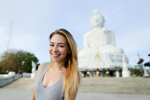 Young blonde girl standing with Buddha statue in Phuket, Thailand. Concept of traveling to Asia and buddhism landmark.