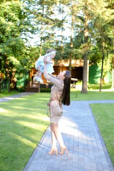 Young brunette mother wearing dress holding little baby in garden. Concept of motherhood and resting on open air in park.