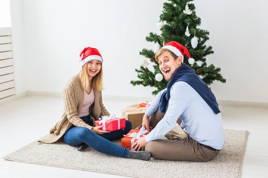 Holidays, relationship and festive concept - Couple opening present together by Christmas tree.