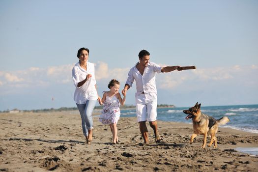 happy young family in white clothing have fun and play with beautiful dog at vacations on beautiful beach 