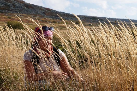 portrait of a woman in tall dry grass against a background of mountains.