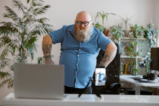 Playful bearded plump man in blue blue shirt shoots new video for blog using mobile phone at home. Entertainment content creating