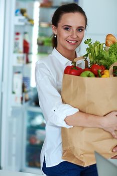 Young woman holding grocery shopping bag with vegetables .Standing in the kitchen.