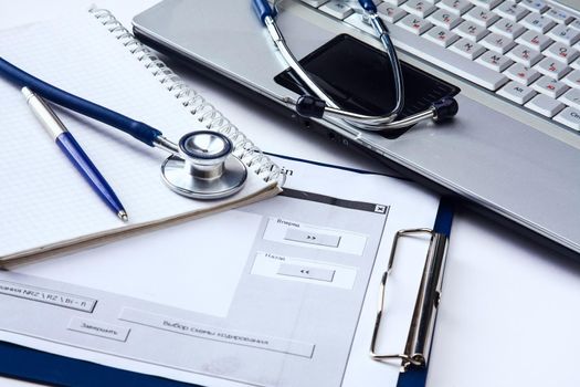 Stethoscope with clipboard and laptop on the desk.