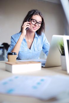 Beautiful young business woman sitting at office desk and talking on cell phone. Business woman.