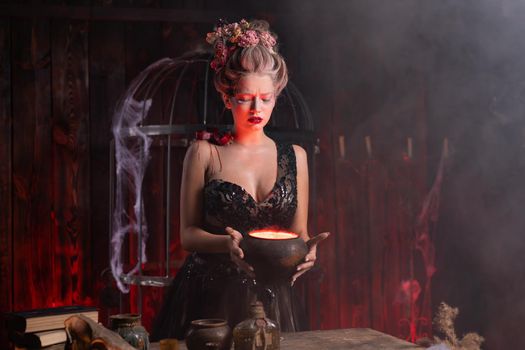 Halloween witch with cauldron. Beautiful young woman conjuring, making witchcraft. Standing spooky dungeon dark room. Enchantress prepare love potion use magic spell