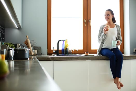 Young woman with cup and cakes sitting in kitchen .