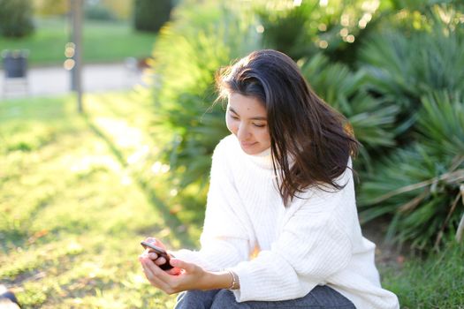 Korean female student sitting in park and typing by smartphone. Concept of modern technology and social networks.