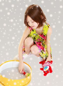 Cute little skinny girl plays with a round box.Gray background with round white snowflakes.