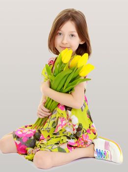 Adorable little Caucasian girl in summer dress holding a bouquet of yellow tulips.On the background of summer blue sky and fluffy clouds.