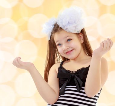 Beautiful, chubby, long-haired little girl with big white bows on the head . girl gesturing with his hands. Close-up.On a brown blurred background with white snowflakes.
