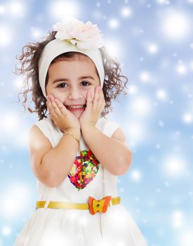 Beautiful little curly girl in a white dress happily surprised. Girl holding hands near the face. Close-up.Blue winter background with white snowflakes.