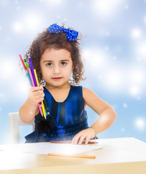 Cute little girl in blue dress, holds a lot of pencils . She paints at a table in a Montessori kindergarten.Blue winter background with white snowflakes.