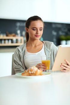 Young woman with orange juice and tablet in kitchen.