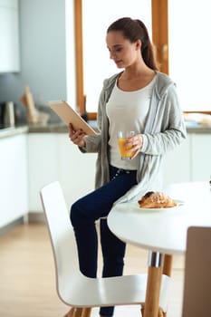 Young woman with orange juice and tablet in kitchen.