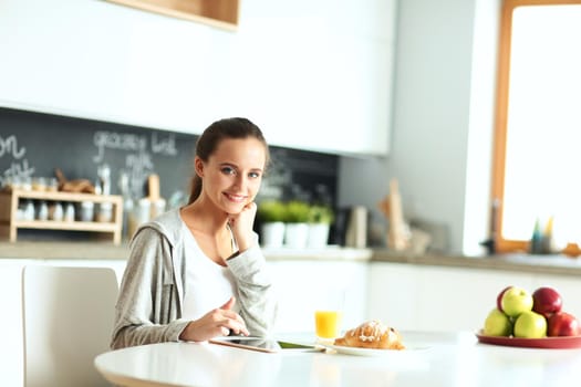 Young woman with orange juice and tablet in kitchen.