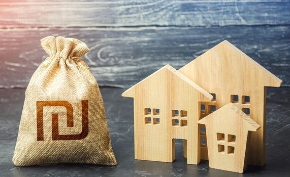 Israeli shekel money bag and figurines of residential buildings. Property tax. Financing urban development and infrastructure projects. Municipal budgeting. Increase investment attractiveness